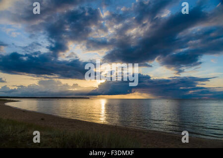 Sonnenuntergang Strahlen durch dramatische Wolken über ruhige See und Strand Stockfoto