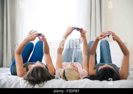 Porträt von einem drei Mädchen auf dem Bett liegend und mit Smartphones zu Hause Stockfoto