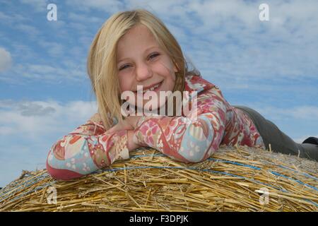 Blonde Mädchen, neun Jahre alt, liegend auf Heuballen, Ystad, Scania, Schweden Stockfoto