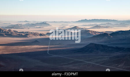 Vereinzelte Bergrücken und C27 gravel Road, Rand der Namib-Wüste, Küstennebel hinter, Luftaufnahme, NamibRand Nature Reserve Stockfoto