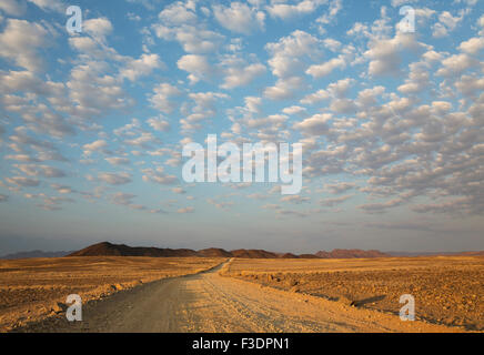 Schotterstraße auf trockenen Ebene, isolierte Bergrücken, flauschigen Wolken am Rande der Namib Wüste, Abendlicht Stockfoto