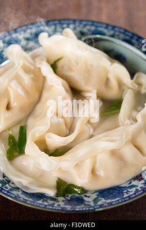 Frische Knödel Suppe auf Teller mit heißen Dämpfe hautnah. Chinesische Küche auf alten Vintage Holz-Hintergrund. Stockfoto