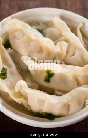 Frische Knödel Suppe auf Teller mit heißen Dämpfe hautnah. Chinesisches Essen auf alten Vintage Holz-Hintergrund. Stockfoto