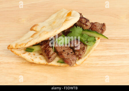 Minute Steak mit Koriander und Gurken in einem Fladenbrot auf einem Holzbrett Stockfoto