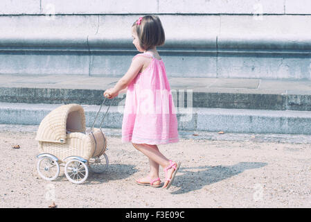 Kleines Mädchen Spielzeug Kinderwagen schieben Stockfoto