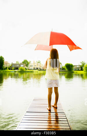 Junge Mädchen mit Regenschirm am Ende See Pier stehen Stockfoto