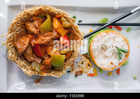 Chinesisches Gericht; Huhn mit grünen Paprikaschoten in einem Nest gebratene Nudeln und gedämpfter Anstieg dekoriert mit Gurke und Karotte beiseite Stockfoto