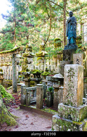 Japan, Koyasan Friedhof, Okunoin. Statue des Priesters auf großen Grabstein, mit torii Tor, Grabsteine und fünf Stein Pagoden im Zedernwald. Stockfoto