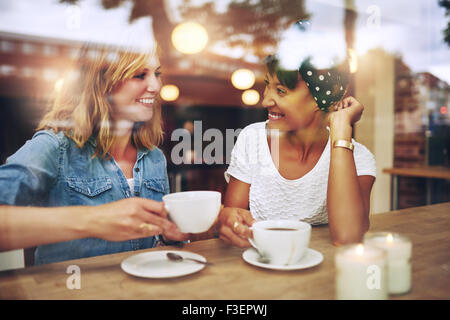 Zwei Multi ethnischen Freunden Kaffeegenuss zusammen in einem Café angesehen durch Glas mit Reflexionen, wie sie an einem Tisch sitzen Stockfoto