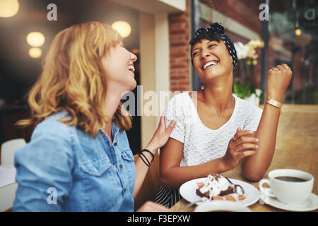 Zwei multiethnischen junge Freundinnen genießen Kaffee zusammen in einem Restaurant Lachen und scherzen beim Berühren Affe anzeigen Stockfoto