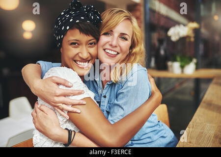 Zwei glückliche liebevolle junge Frau umarmen einander in einer engen Umarmung beim Lachen und Lächeln, junge multirassische weibliche fr Stockfoto