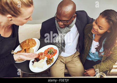 Kellnerin mit vergoldeten Küche für junge afrikanische amerikanische Kunden in einem Restaurant, erhöhte Ansicht zeigt das Essen auf den Tellern Stockfoto