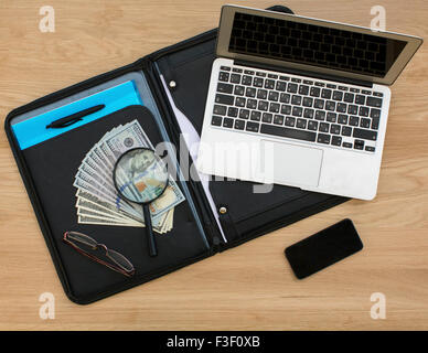 Business-Ordner mit Dollarnoten, geöffnet Laptop und Smartphone auf Holztisch Oberfläche. Stockfoto