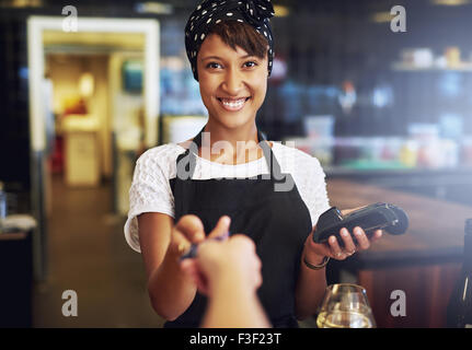Lächelnd Kellnerin oder Inhaber eines kleinen Unternehmens nehmen eine Kreditkarte von einem Kunden, durch die Banken-Maschine in Zahlung zu verarbeiten Stockfoto