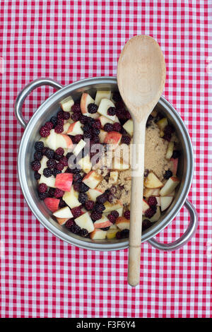 Pfanne von gesammelten Brombeeren und Äpfel mit Zucker und einem Holzlöffel auf eine karierte Tischdecke Stockfoto