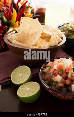 Frische Tortillachips mit Pico de Gallo und frischen Limetten in Vordergrund, Guacamole und Margarita im Hintergrund. Stockfoto