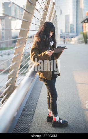 junge schöne asiatische lange braune glatte Haare Frau mit einem Tablet online verbunden in der Stadt während des Sonnenuntergangs bei Gegenlicht- Stockfoto