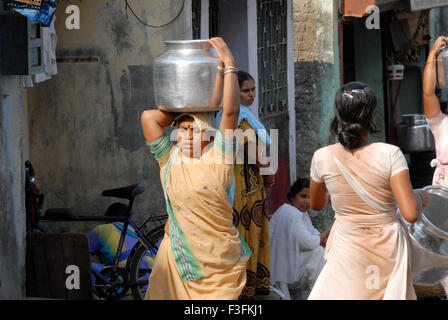 Frauen tragen auf dem Kopf in einem Slum in Chembur Trinkwasser in Aluminium-Behälter; Bombay jetzt Mumbai; Maharashtra; Indien Stockfoto