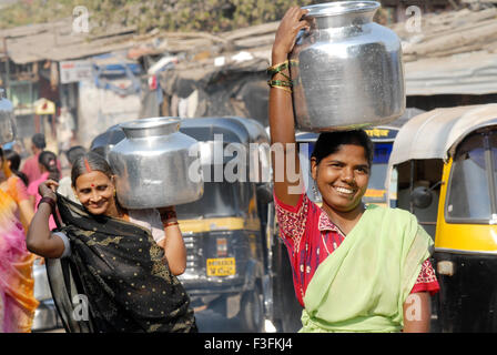 Frauen tragen auf dem Kopf in einem Slum in Chembur Trinkwasser in Aluminium-Behälter; Bombay jetzt Mumbai; Maharashtra; Indien Stockfoto