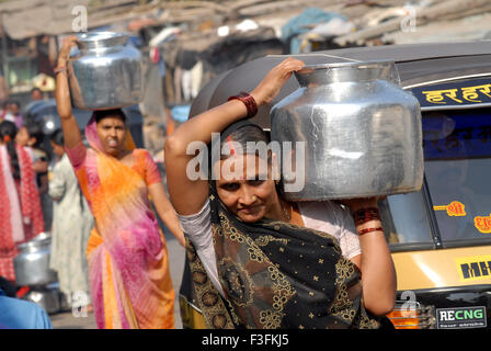 Frauen tragen auf dem Kopf in einem Slum in Chembur Trinkwasser in Aluminium-Behälter; Bombay jetzt Mumbai; Maharashtra; Indien Stockfoto