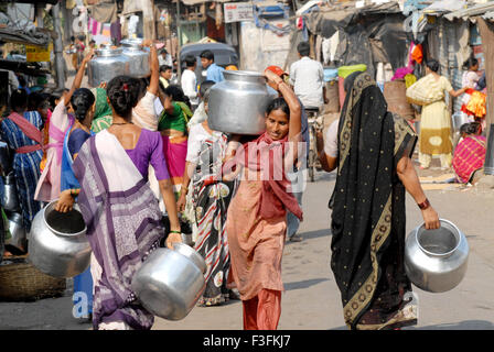 Frauen tragen auf dem Kopf in einem Slum in Chembur Trinkwasser in Aluminium-Behälter; Bombay jetzt Mumbai; Maharashtra; Indien Stockfoto