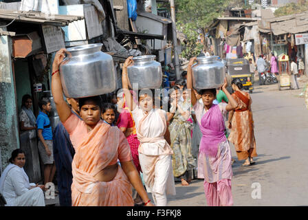 Frauen tragen auf dem Kopf in einem Slum in Chembur Trinkwasser in Aluminium-Behälter; Bombay jetzt Mumbai; Maharashtra; Indien Stockfoto