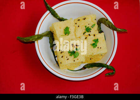 Vier Stücke von gelben Khaman oder Dhoklas mit gebratene grüne Chilis in Schale serviert Stockfoto