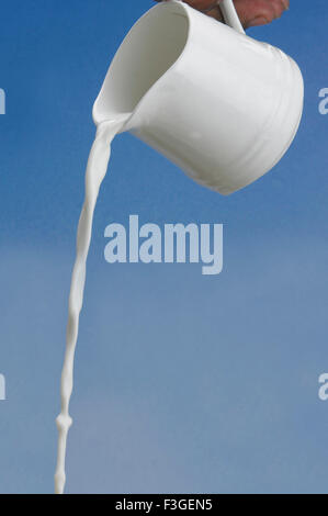 Zu trinken; Hand hält Krug und gießen Milch auf blauem Hintergrund Stockfoto
