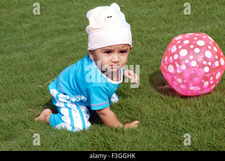 Baby krabbeln tragen weiße Kappe in blauem Kleid spielen mit rosa Kunststoff Kugel auf grünem Gras MRr #152 Stockfoto