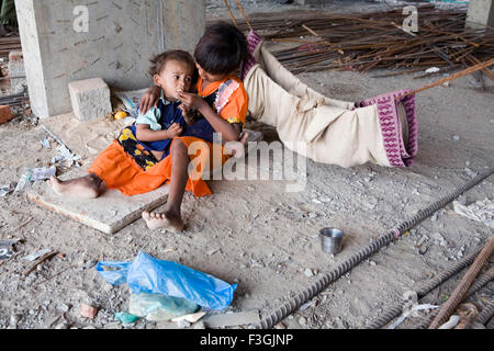 Ein junges Mädchen füttert ihre Geschwister auf einer Baustelle, während ihre Eltern Weg auf Arbeit sind; Ahmedabad; Gujarat; Indien Stockfoto