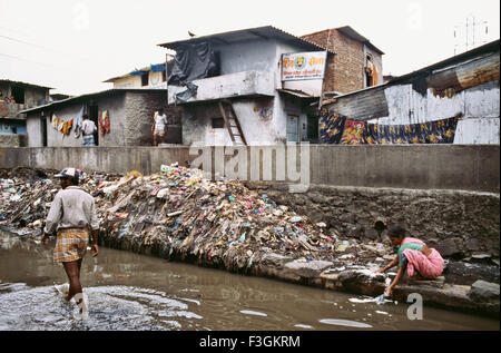 Frau, die Tuch im schmutzigen Wasser entlang eines Kanals wäscht, der mit Abfall in einem Slum in Bombay jetzt Mumbai gedumpt wird; Maharashtra; Indien; Asien Stockfoto