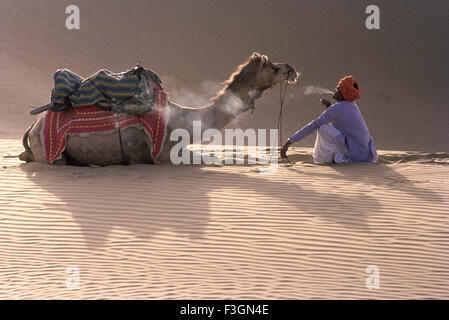 Rajasthani Mann Rauchen sitzend vor Kamel in der Wüste ruhen; Bikaner; Rajasthani; Indien Herr Stockfoto