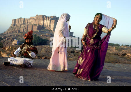 Volkstänzer; Rajasthani Frauen tanzen und Mann spielen Musikinstrument Mehrangarh Fort im Hintergrund; Jodhpur Stockfoto