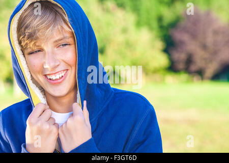 Glücklich lachende männliche junge blonde Teenager Kind außerhalb in Sommersonne tragen eine blaue hoody Stockfoto