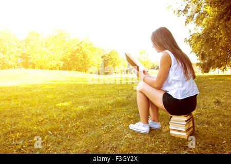 Attraktive weibliche College-Student, ein Buch lesen und sitzen auf den Bücherstapel. Bildung. Zurück zu Schule Konzeptbild. Stockfoto