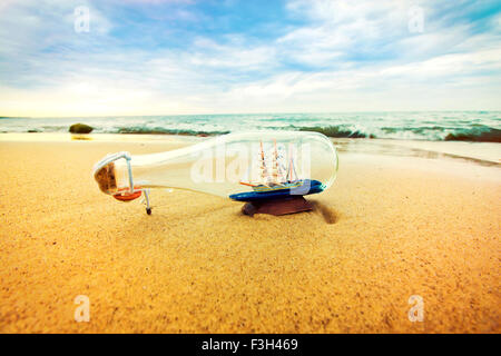 Flasche mit Schiff innen am Strand liegen. Souvenir-Konzeptbild. Natur im Paradies. Stockfoto