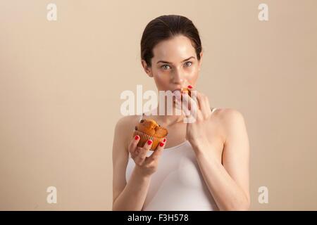 Porträt der jungen Frau einen Muffin Essen Blick in die Kamera Stockfoto