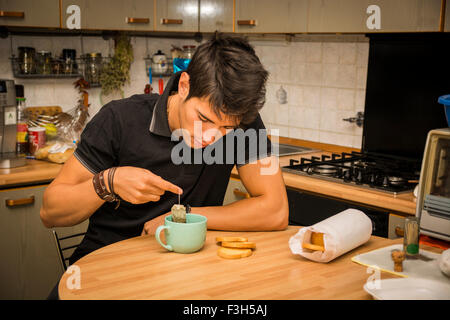 Müde oder krank attraktive junge Mann gelehnt mit Ellenbogen am Küchentisch und halten Tasse Kaffee zum Frühstück Stockfoto