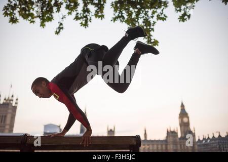 Junger Mann springen über Parkbank am Southbank, London, UK Stockfoto