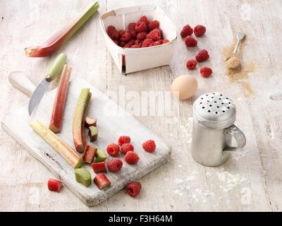 Zutaten für Rhabarber und Himbeeren Schuster Pudding auf weiß getünchten Holztisch Stockfoto