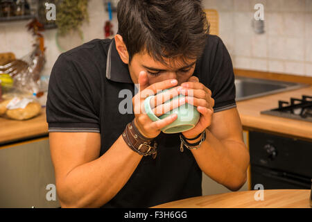 Müde oder krank attraktive junge Mann gelehnt mit Ellenbogen am Küchentisch und halten Tasse Kaffee zum Frühstück Stockfoto