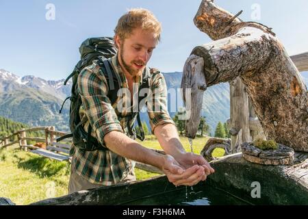 Junge männliche Wanderer Trinkwasser aus rustikalen Trog, Karthaus, Val Senales, Südtirol, Italien Stockfoto