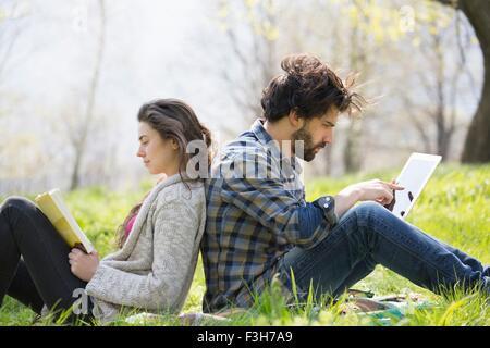 Junges Paar Rücken an Rücken auf der Picknickdecke mit digital-Tablette und lesen Stockfoto