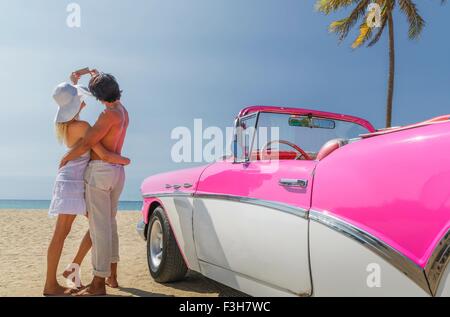 Paar nehmen Selfie mit Smartphone neben Cabrio am Strand Stockfoto