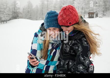 Junge Frauen mit Smartphone lächelnd in Schnee, Sattelbergalm, Tirol, Österreich Stockfoto