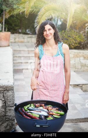 Porträt von Reife Frau bereitet Grillgerichte auf Terrasse Stockfoto
