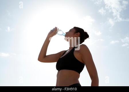 Niedrigen Winkel Blick auf blauen Himmel und Mitte erwachsenen Frau trinkt Mineralwasser Stockfoto