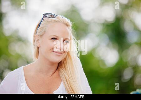 Porträt der langhaarige blonde junge Frau mit Sonnenbrille auf dem Kopf aussehende Weg lächelnd Stockfoto