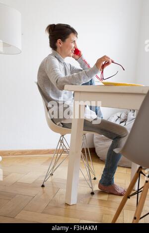 Seitenansicht des Reife Frau am Tisch reden auf roten Festnetz-Telefon Stockfoto