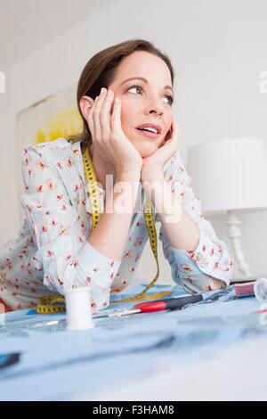 Reife Frau mit Maßband ruht auf Ellbogen, Kinn auf Händen wegschauen Stockfoto